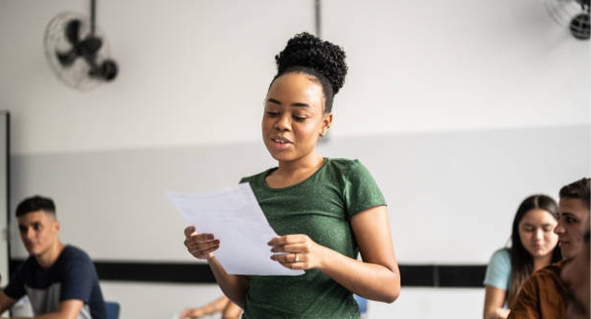 A STRACS tutor leading a public-speaking exercise in front of students in a classroom